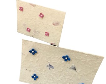 Peut inclure: Deux cartes en papier faites à la main avec une surface texturée blanc cassé. L'une des cartes présente des ornements de fleurs roses, l'autre des accents de fleurs bleues. Les cartes ont une esthétique rustique et naturelle.