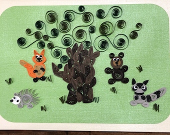Peut inclure: Carte d'art en papier quilling faite à la main représentant une scène de forêt fantaisiste. La carte présente un arbre avec un tronc brun et des feuilles vertes tourbillonnantes, entouré d'un renard, d'un ours, d'un hérisson et d'un raton laveur. Le fond est vert clair.