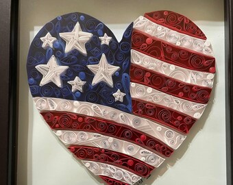Peut inclure: Une œuvre d'art encadrée en forme de cœur représentant le drapeau américain, réalisée en quilling. Elle présente des rayures rouges et blanches, un champ bleu avec des étoiles blanches, le tout dans un cadre noir. Un objet décoratif patriotique.