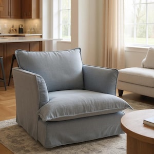 May include: A light blue armchair with a slipcovered design, featuring a deep seat cushion, a tall back cushion, and wide armrests. The chair is upholstered in a textured fabric and sits low to the ground with a skirted base covering the frame.