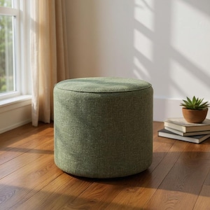 Può includere: Un pouf cilindrico rivestito in un tessuto testurizzato color verde salvia. L'oggetto presenta una superficie superiore circolare piatta e lati verticali dritti, caratterizzati da una finitura in materiale intrecciato di colore uniforme.