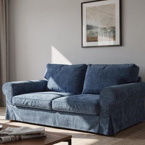 May include: A blue corduroy sofa with two cushions and rolled arms. The sofa is in a living room setting with a coffee table, a cup of coffee, and a framed picture on the wall. Sunlight streams in from a nearby window.