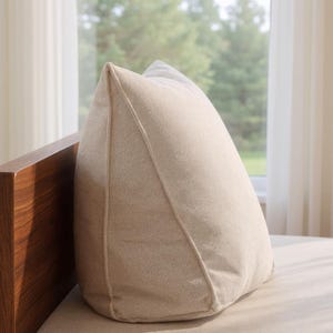 Peut inclure: Un coussin en forme de coin de couleur beige clair uni avec une finition en tissu texturé. Le coussin présente une couture verticale distincte le long du bord avant, créant un profil triangulaire structuré conçu pour le soutien.