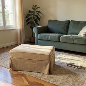 Könnte beinhalten: Wohnzimmer mit grünem Sofa, beigem Hocker und gemustertem Teppich. Ein Fenster mit transparenten Vorhängen lässt natürliches Licht herein. Eine Topfpflanze fügt einen Hauch von Natur hinzu. Warme, einladende Atmosphäre.