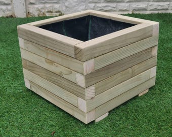Puede incluir: Una jardinera cuadrada de madera con un forro marrón oscuro. La jardinera está hecha de madera natural con un acabado marrón claro y tiene un diseño simple y rústico.