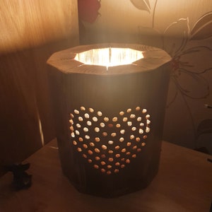 May include: A wooden lamp with a heart-shaped cutout design. The lamp is lit and casting a warm glow.