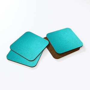 May include: Set of four turquoise blue square coasters with a textured surface. The coasters have a brown cork backing.