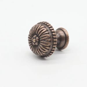 May include: A copper-toned cabinet knob with a decorative floral design. The knob has a round base and a short, cylindrical stem.