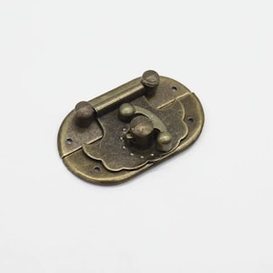 May include: Antique brass latch with a decorative floral design. The latch has a small knob for opening and closing.