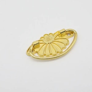 May include: Gold metal drawer pull with a decorative flower design. The pull has a rounded shape and a smooth finish.