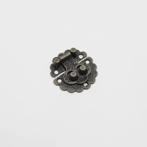 May include: Antique brass latch with a decorative floral design. The latch has a round shape and a hinged mechanism.