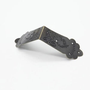 May include: Antique brass corner bracket with a decorative design of a bird and flower. The bracket has a scalloped edge and is perfect for adding a touch of vintage charm to furniture or crafts.