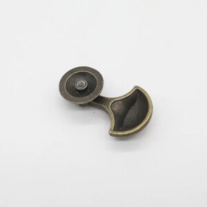 May include: A bronze-toned metal drawer pull featuring a circular mounting base with a central threaded hole and a curved, fan-shaped handle extension. The hardware has a weathered, dark metallic finish with visible highlights on the edges.