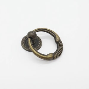 Pode incluir: Puxador de porta de armário de anel de latão antigo com um design decorativo de corda. O puxador tem uma base redonda com uma borda decorativa.
