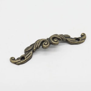 May include: A decorative antique gold-toned metal drawer pull with a scroll design.