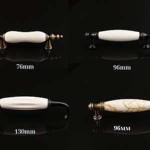 Könnte beinhalten: Vier Schrankgriffe mit weißen Keramikgriffen. Die Griffe haben verschiedene Metallausführungen, darunter Messing und Schwarz. Maße sind 76 mm, 96 mm und 130 mm. Die Keramikgriffe haben einen Craquelé- oder Marmoreffekt.