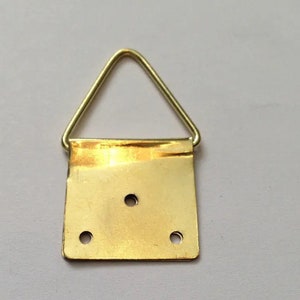 May include: A gold-colored metal picture hanging hook with a triangular loop and three holes.