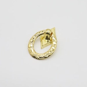 May include: Gold-toned metal ring pull with a decorative floral design. The ring pull is attached to a diamond-shaped plate.