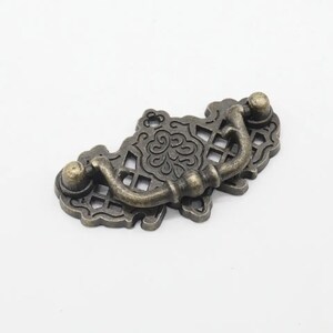 May include: An ornate, antique-style cabinet pull with a decorative, openwork design. The pull is made of metal and has a dark bronze finish.