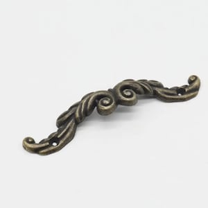 May include: A decorative metal drawer pull with a scroll design in an antique bronze finish.