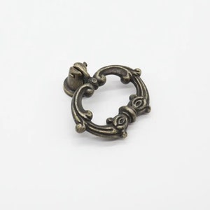 May include: A decorative antique brass cabinet pull with a ring handle and ornate details.