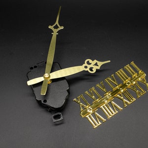 Puede incluir: Manecillas de reloj doradas y esfera de reloj con números romanos para un kit de reloj. Las manecillas están unidas a un mecanismo de reloj negro.