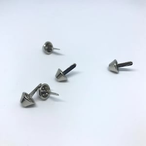 May include: Four silver-toned metal cone-shaped rivets with a pointed end and a flat top. The rivets are scattered on a white surface.