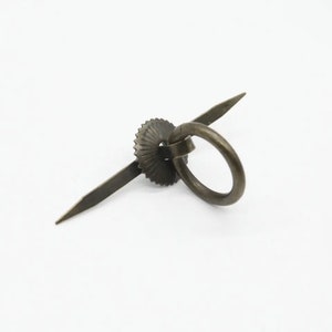 May include: A bronze ring pull handle with a decorative, scalloped, circular base. The handle is attached to the base with a metal rod.