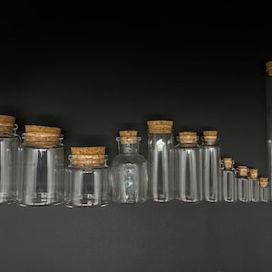 May include: A collection of clear glass jars and vials of varying sizes and shapes, each topped with a natural brown cork stopper. The containers are arranged in a row, ranging from wide, short jars to tall, slender test tube-style vials.