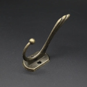 May include: A single antique gold-toned metal hook with a decorative swirl design. The hook has a rounded base with two screw holes.