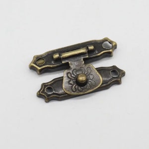 May include: Antique brass latch with a decorative floral design and a round button. The latch has two holes for mounting.