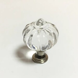May include: Clear glass cabinet knob with a ribbed, pumpkin-shaped design. The knob sits on a silver-toned base. This decorative hardware is suitable for drawers, cabinets, or furniture.