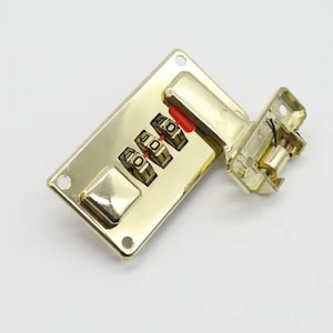 Può includere: Lucchetto a combinazione dorato con tre quadranti impostati su 401. Il lucchetto è fissato a una piastra metallica con due fori.