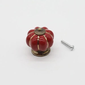 May include: Red ceramic pumpkin-shaped cabinet knob with gold accents and a matching screw.