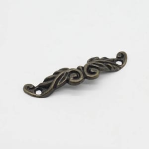 May include: A decorative metal pull handle with a scroll design in an antique bronze finish.