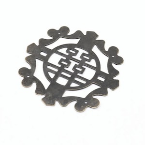 May include: A decorative metal ornament in the shape of a circle with a stylized design inside. The ornament is made of brass and has a dark, antique finish.