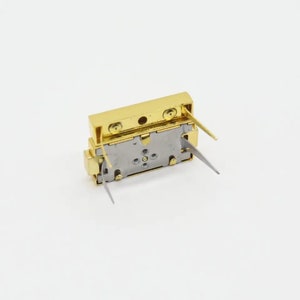 May include: A gold-colored electronic component with four metal pins. The component has a rectangular shape and a silver-colored base.