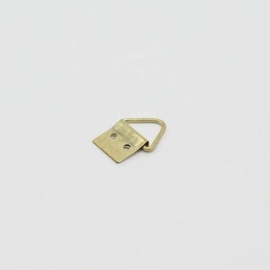 May include: A gold-toned metal picture hanging hook with a triangular base and a D-shaped ring.