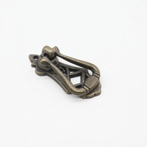 May include: Antique brass cabinet pull with a decorative, openwork design. The pull has a ring handle and a decorative, ornate base.
