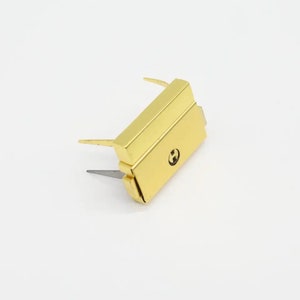 May include: Gold-colored metal clasp with two prongs and a small, round, engraved 'H' on the front.