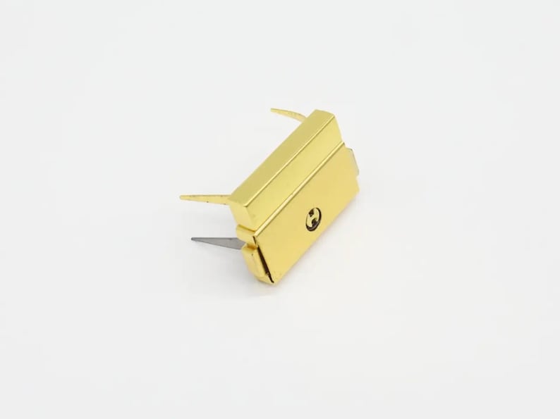 May include: Gold-colored metal clasp with two prongs and a small, round, engraved 'H' on the front.