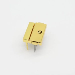 May include: Gold-toned metal clasp with a small screw in the center. The clasp has two prongs extending from the bottom.