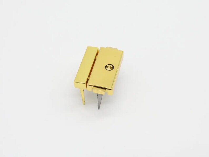 May include: Gold-toned metal clasp with a small screw in the center. The clasp has two prongs extending from the bottom.