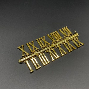 May include: Gold Roman numeral clock numbers on a strip. The numbers are arranged in order from I to XII.