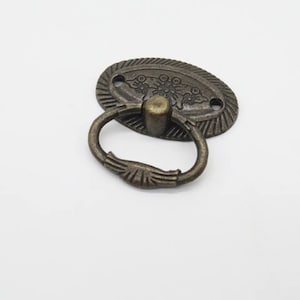 Op de afbeelding: Antieke ovale bronzen kastgreep met een decoratief bloemmotief en een ringgreep.