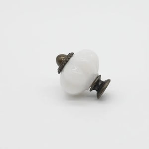 May include: White ceramic cabinet knob with a brass base and a decorative ring around the top.