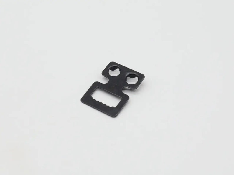 May include: Black metal buckle with two holes and a slot for a strap.