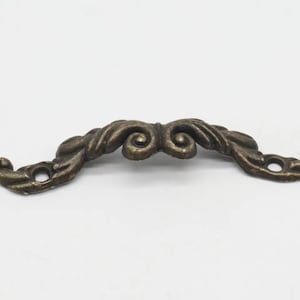 May include: A decorative bronze-coloured metal drawer pull with a scroll design.