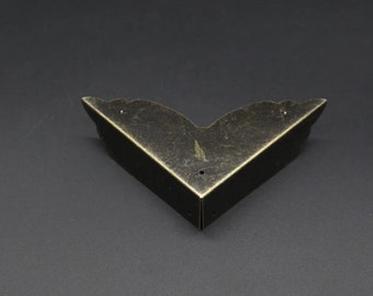 May include: A V-shaped metal corner protector with an antique bronze finish. The piece features a decorative scalloped edge along the top and includes three small pre-drilled holes for mounting, designed to fit onto the corner of a box or furniture.