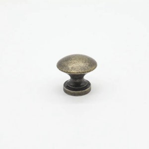 May include: A round cabinet knob with a distressed antique brass finish. The knob features a smooth, domed top surface that tapers down into a narrow neck, ending in a circular base. The metal has a textured, weathered appearance throughout.